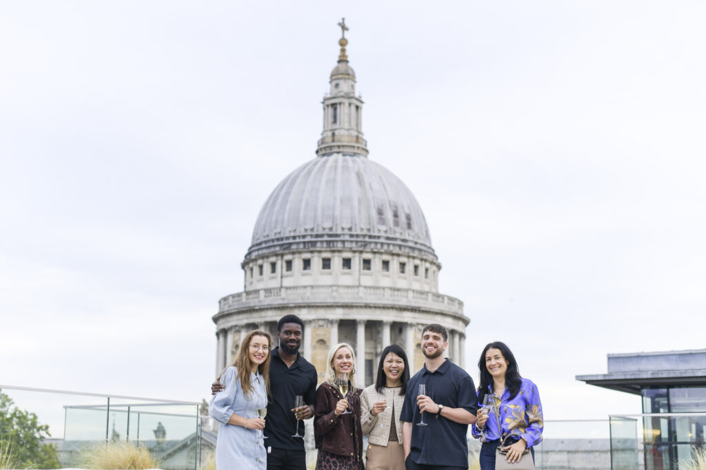 5 people standing in front of St Paul's Cathedral, holding wine glasses and smiling.