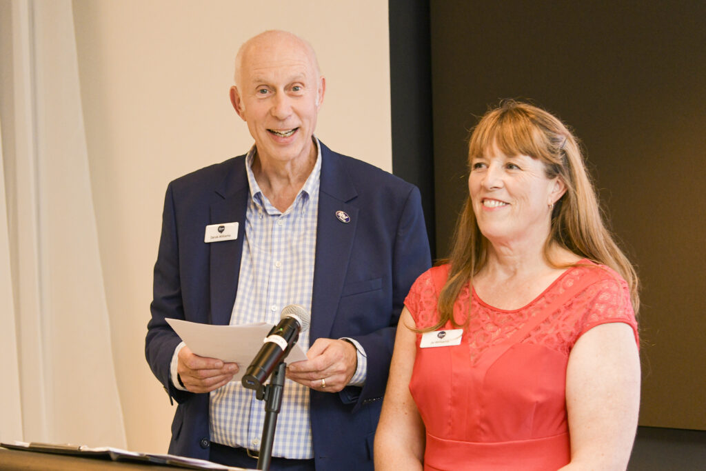 Man in navy blazer smiling next to woman in red dress.