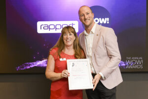 Woman in red dress with man in light coloured blazer, holding a certificate in front of WOW! Awards and Rapport logo.