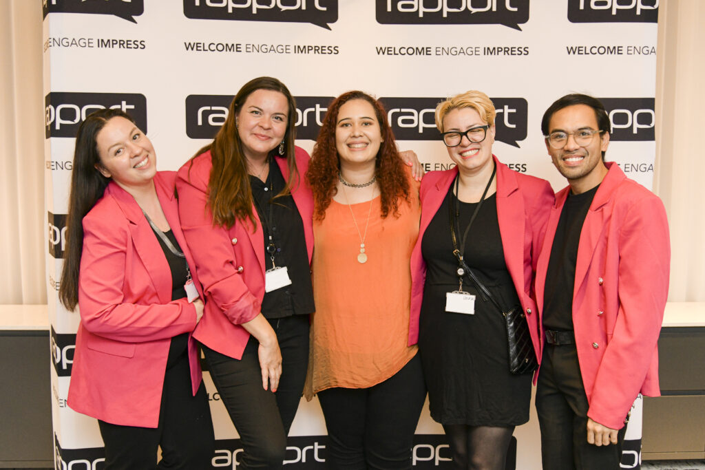5 women in pink jackets smiling to camera, in front of Rapport backdrop.